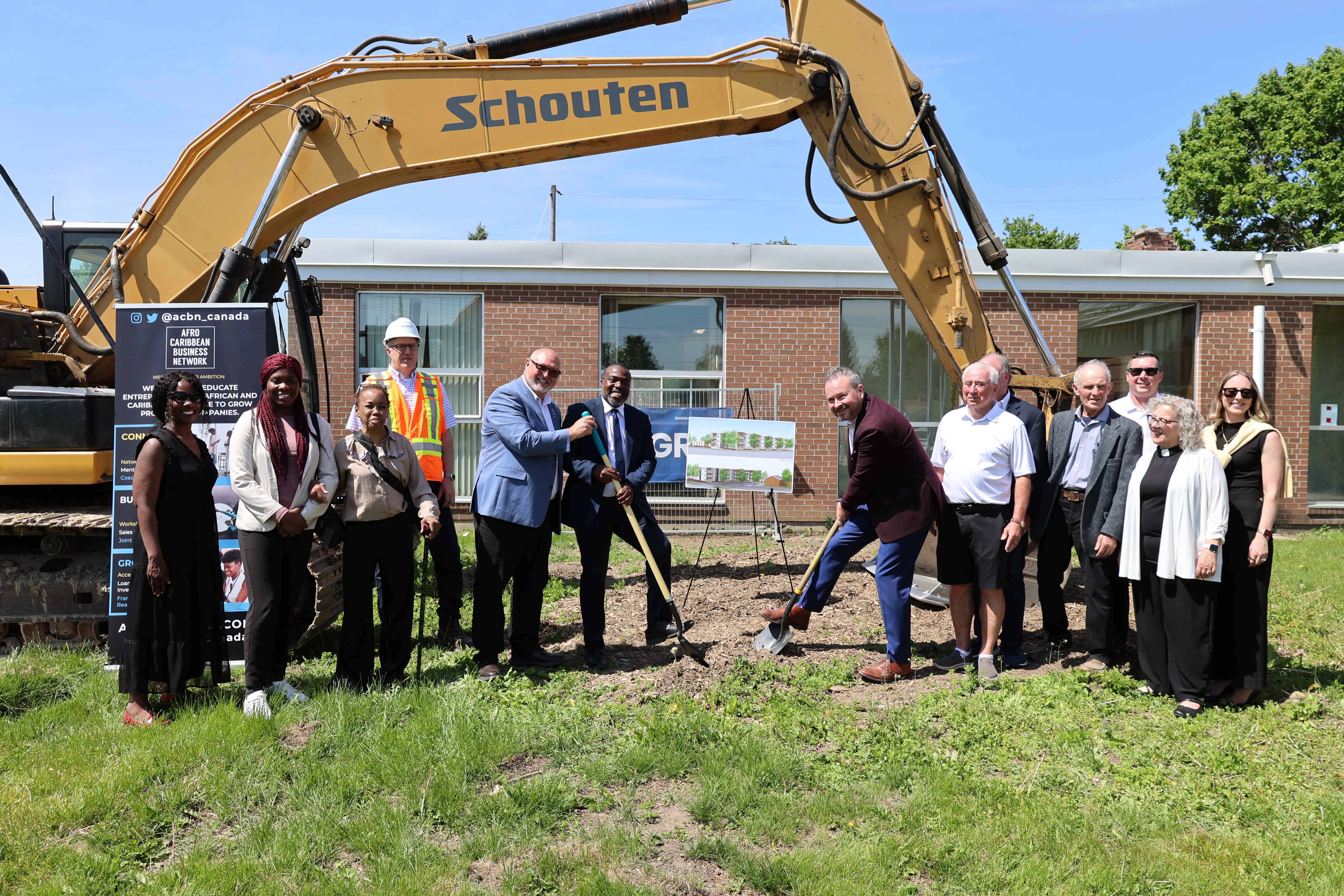 Group photo with shovels in the ground under an excavator