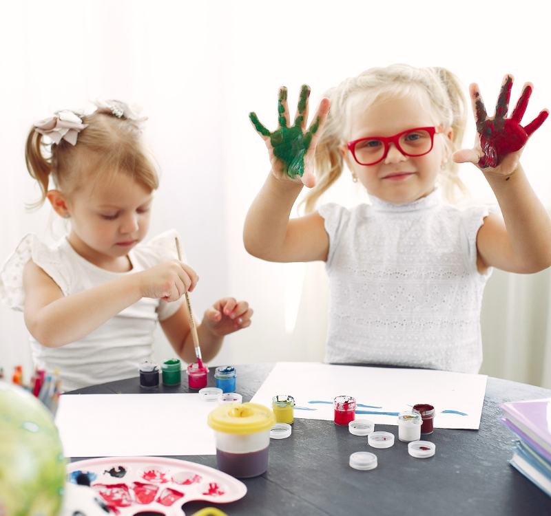 Two young girls painting, with paint on their hands