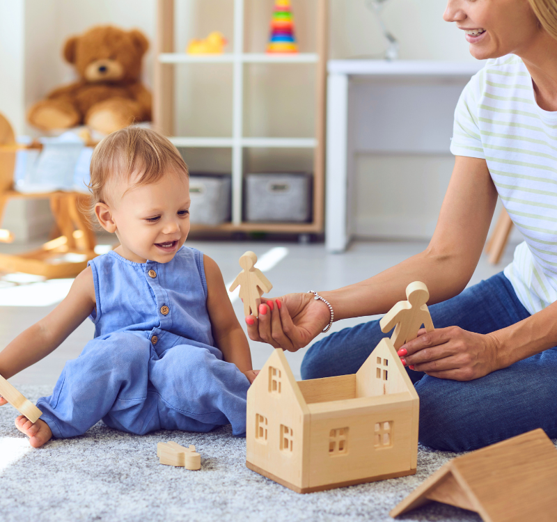 Small child playing with a wood house and care provider