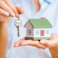 A hand holding a little toy house and a key hanging in the other hand